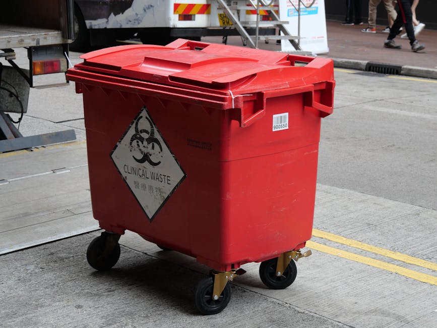 A collection of large plastic containers and bottles in various colors—blue, red, yellow, and black—are shown stacked outdoors on a garden surface, with some containers having labels or markings.